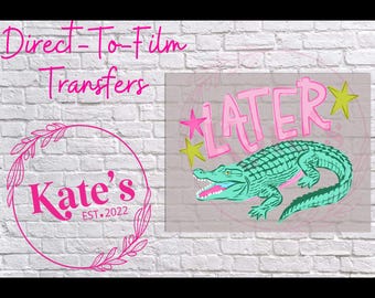 May include: A graphic design featuring a green alligator with the word "LATER" in pink, accented with pink stars and yellow stars. The image also includes the text "Direct-To-Film Transfers" and a pink circular logo with the text "Kate's EST.2022".