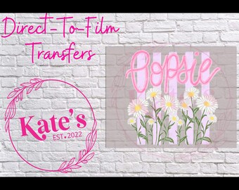 May include: A pink and white graphic featuring the word "Popsie" in cursive over a field of daisies. The image also includes the text "Direct-To-Film Transfers" and a circular logo with the text "Kate's EST.2022".