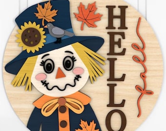 May include: A round wooden sign featuring a scarecrow design with a navy blue hat adorned with a sunflower and fall leaves. The word "HELLO" is displayed in brown letters. A decorative orange swirl and a jute rope complete the fall-themed decor.