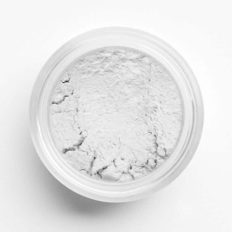 May include: A small, round, clear glass jar filled with a white powder. The powder is smooth and has a slightly grainy texture.