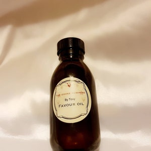 May include: A brown glass bottle with a black cap and a white label that reads "The Divine Feminine By Toxxy Favour Oil".