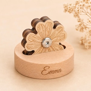 May include: A light-colored wooden circular base with the name Emma engraved on the front. A layered wooden flower cutout with a silver metal center is inserted into a slot on the top of the base. The flower features etched petal details.