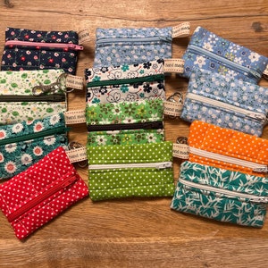 May include: A collection of 10 small zippered pouches with various floral and geometric patterns. The pouches are made of fabric and have a key ring attached. The pouches are all hand-made.