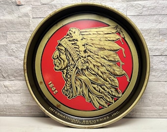 May include: Vintage round metal tray with a red and gold design. The tray features a profile of a Native American chief with the word "IROQUOIS" and the number "1842". The tray is from "INTERNATIONAL BREWERIES INC. BUFFALO, N.Y."