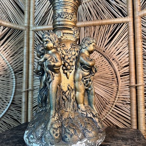 May include: A gold-painted lamp base with cherub figures and grapevine accents. The base is made of plaster and has a distressed finish.