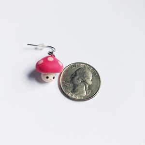 May include: A pink and white mushroom with a cute face, hanging from a silver earring hook. The mushroom is about the size of a US quarter.