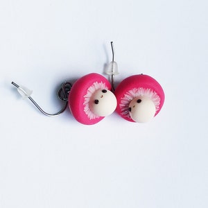 May include: A pair of pink mushroom earrings with white faces and black eyes. The earrings are made of polymer clay and have silver hooks.