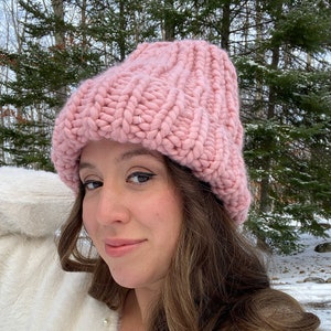 Peut inclure: Un bonnet en tricot rose avec une coupe ample. Le bonnet est fait avec un fil épais et a une texture côtelée.