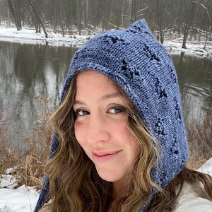 Peut inclure: Un bonnet à capuche en tricot bleu avec un motif ajouré. Le bonnet a une longue ficelle qui pend devant.