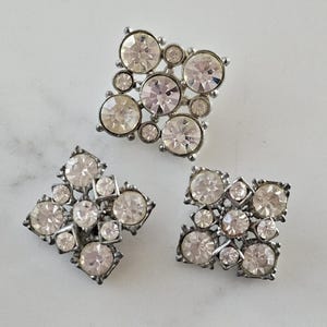 May include: Three silver-toned, square-shaped brooches with clear rhinestone embellishments.