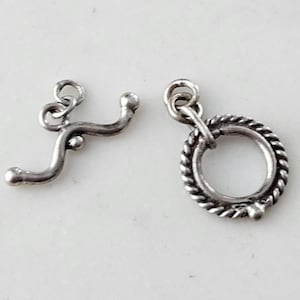 May include: Two silver metal clasps for jewelry making. One clasp is a simple loop with a curved bar. The other clasp is a round ring with a rope-like design.