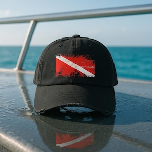 May include: Black baseball cap featuring a distressed red and white scuba diving flag design.