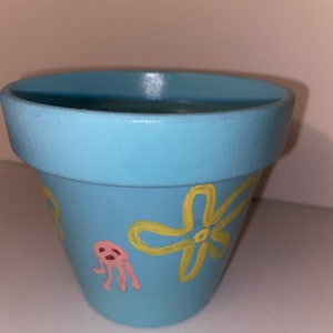 May include: A light blue ceramic planter with a yellow flower and a pink jellyfish painted on it.