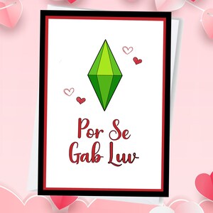 May include: A white card with a red border and a black border. The card has a green diamond shape with a red heart above it. The text "Por Se Gab Luv" is written in red cursive on the card.