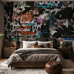 May include: A bedroom featuring a bed with a taupe duvet and pillows, positioned against a wall covered in a collage of torn posters, graffiti, and street art in black, white, orange, and teal. A brown leather pouf sits at the foot of the bed.