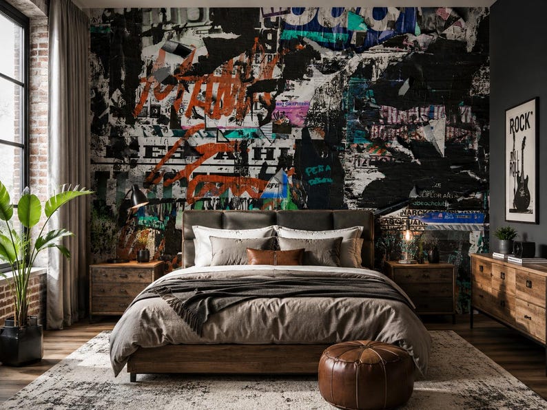 May include: A bedroom featuring a bed with a taupe duvet and pillows, positioned against a wall covered in a collage of torn posters, graffiti, and street art in black, white, orange, and teal. A brown leather pouf sits at the foot of the bed.
