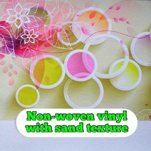 May include: Wallpaper with an abstract floral design. It features pink, yellow, and orange circles with white outlines against a light beige, sand-textured background. The text "Non-woven vinyl with sand texture" is displayed at the bottom.