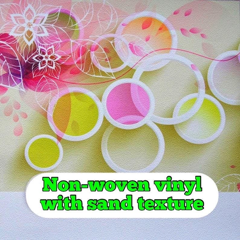 May include: Wallpaper with an abstract floral design. It features pink, yellow, and orange circles with white outlines against a light beige, sand-textured background. The text "Non-woven vinyl with sand texture" is displayed at the bottom.