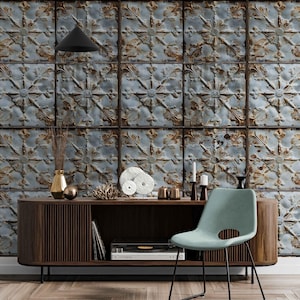 Op de afbeelding: Een vintage-geïnspireerd behang met een herhalend patroon van blauwe en bruine tinnen plafondtegels met een bloemmotief. Het behang wordt getoond in een kamer met een moderne houten consoletafel, een platenspeler en een turquoise stoel.