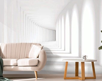 May include: A modern living room scene featuring a light beige sofa with a green blanket and a white pillow. A round side table with wooden legs holds a mug. The wall features a white, geometric design, and a potted plant adds a touch of greenery.