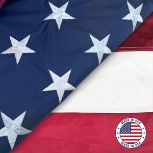 May include: A close-up of a United States flag, featuring a blue field with white embroidered stars and red and white stripes. The flag is partially folded, revealing the "Made in USA" emblem.