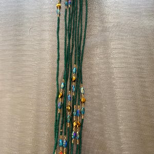 K&ouml;nnte beinhalten: Eine lange Kette aus gr&uuml;nen Perlen mit goldenen und irisierenden blauen Perlen.