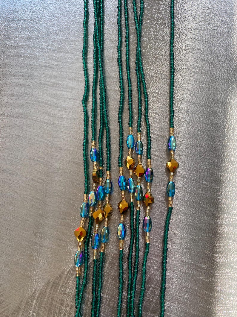 K&ouml;nnte beinhalten: Ein Set aus sieben gr&uuml;nen Perlen f&uuml;r die Taille mit schillernden blauen und goldenen Perlen. Die Perlen sind auf einer d&uuml;nnen Schnur aufgef&auml;delt und etwa 76 cm lang.