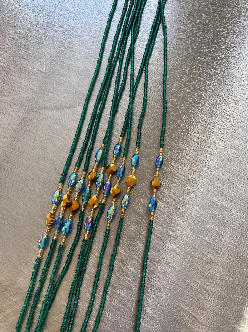 K&ouml;nnte beinhalten: Ein Satz gr&uuml;ner Perlen f&uuml;r die Taille mit goldenen und regenbogenfarbenen blauen Akzenten. Die Perlen sind auf einer d&uuml;nnen Schnur aufgef&auml;delt und etwa 76 cm lang.