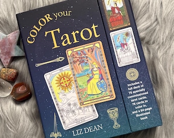 May include: A navy blue tarot card box with the words "COLOR your Tarot" in gold lettering. The box includes a full deck of 78 tarot cards to color in, and a 64-page illustrated book. The box is next to a star-shaped stone and several small crystals.