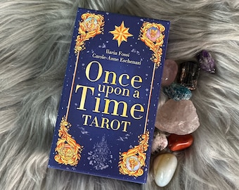 以下が含まれることがあります： イラリア・フォッシとキャロル＝アンヌ・エシェナジによる「Once upon a Time Tarot」というタイトルの青と金のタロットデッキボックス。ボックスはカラフルな宝石で囲まれています。