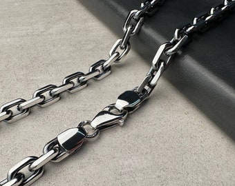 May include: A silver-colored chain necklace with a rectangular link design. The necklace features a secure clasp and is displayed on a neutral background. The chain is made of a shiny, reflective metal.