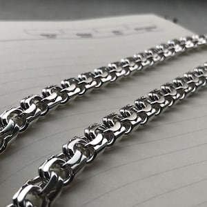 May include: A silver chain necklace with a box chain design. The chain is made of interlocking links that form a square pattern.