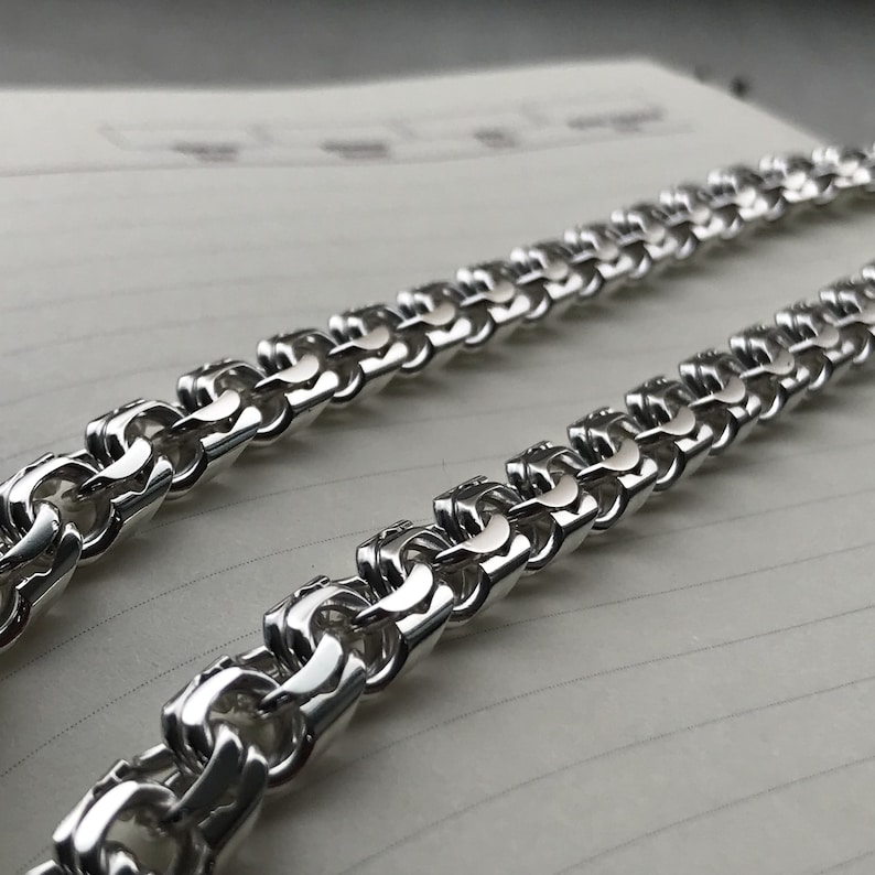 May include: A silver chain necklace with a box chain design. The chain is made of interlocking links that form a square pattern.