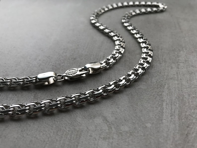 May include: A silver chain necklace with a box chain design. The chain is made of interlocking links that form a square pattern.