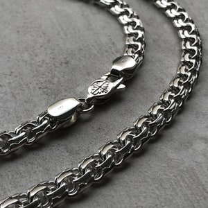 May include: A silver chain necklace with a box clasp. The chain is made of interlocking links that form a woven pattern.