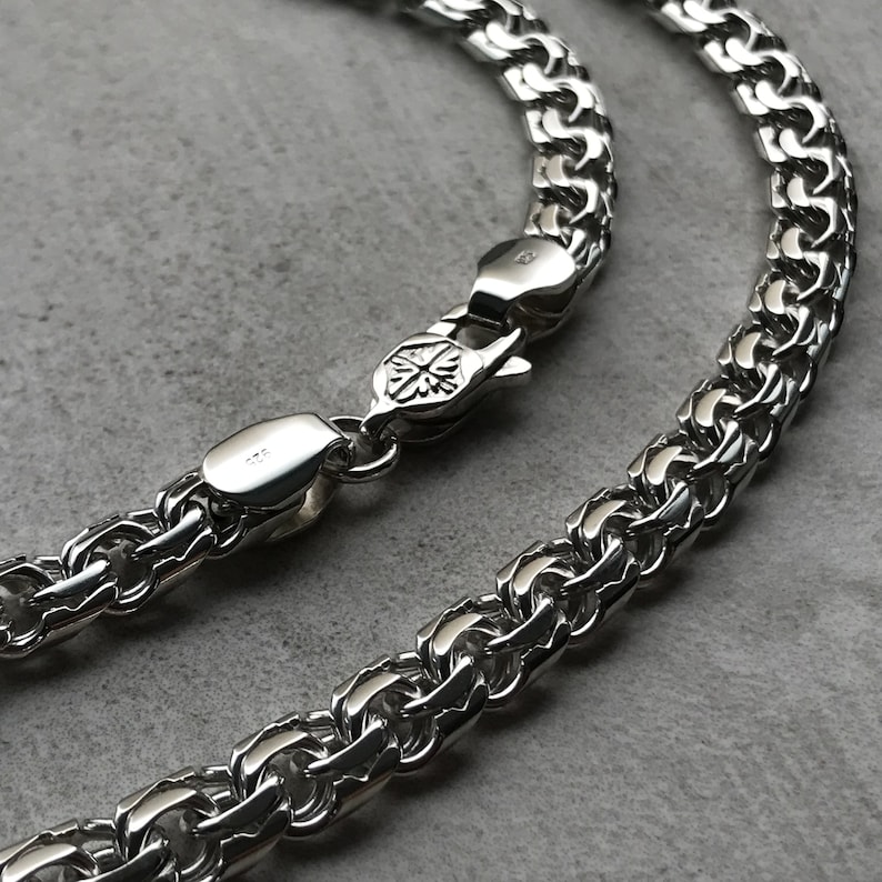 May include: A silver chain necklace with a box clasp. The chain is made of interlocking links that form a woven pattern.