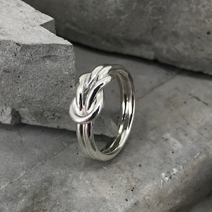 Peut inclure: Une bague en argent en forme de nœud avec une finition polie. La bague est composée de trois brins de métal qui sont torsadés ensemble pour former un nœud.