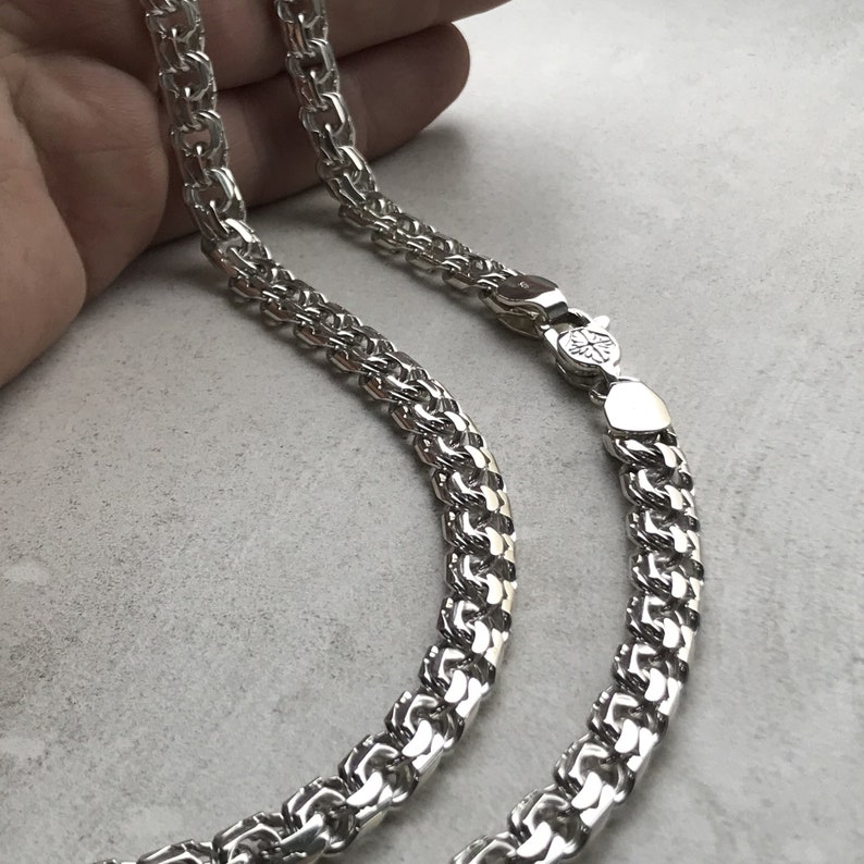 May include: A silver chain necklace with a box chain design. The chain is made of interlocking square links.
