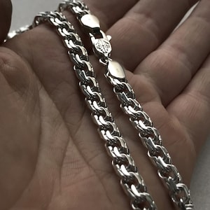 May include: Two silver chains with a curb link design. The chains are laying on a hand.