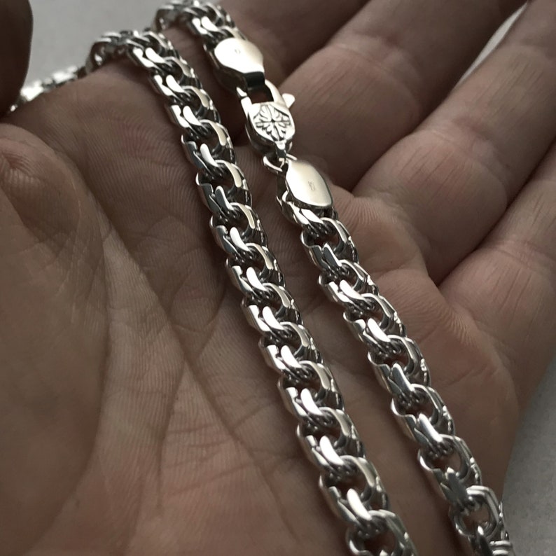 May include: Two silver chains with a curb link design. The chains are laying on a hand.