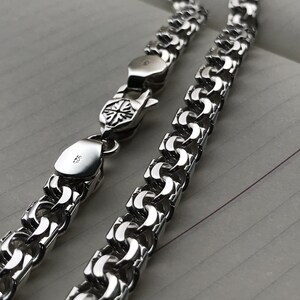 May include: A silver chain necklace with a box clasp. The chain is made of interlocking links that form a woven pattern.