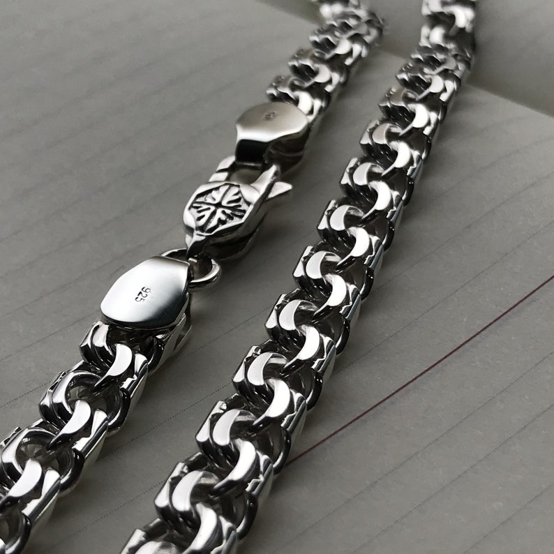 May include: A silver chain necklace with a box clasp. The chain is made of interlocking links that form a woven pattern.