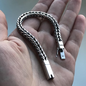 Könnte beinhalten: Ein silbernes Kettenarmband mit geflochtenem Design. Das Armband hat einen Verschluss und ist mit der Nummer "925" gekennzeichnet.