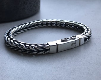May include: A silver chain bracelet with a clasp closure. The bracelet is made of a braided chain design.