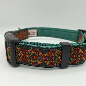 May include: A dog collar with a black base and a decorative pattern in red, orange, and green. The collar has a teal green interior and black plastic hardware. The design features a repeating floral pattern.
