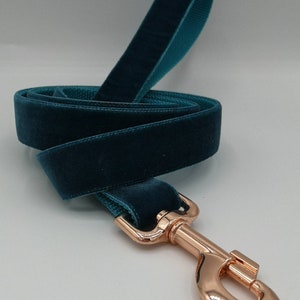 May include: A teal velvet dog leash with a rose gold-colored metal clasp. The leash is made of a soft, plush velvet material and has a matching teal backing. The clasp is a swivel style, designed for easy attachment to a dog's collar.