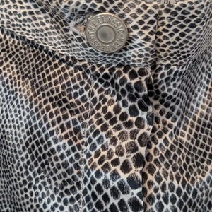 May include: Close-up of a black and white snake skin patterned fabric with a silver button that reads "The Classic - Members Only".