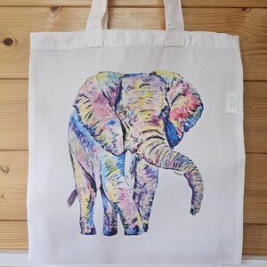 May include: A white tote bag with a colorful illustration of an elephant. The elephant is painted in shades of pink, yellow, blue, and purple.