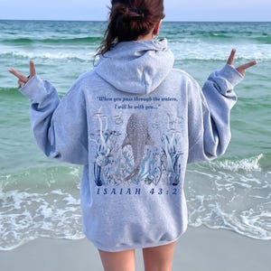 Könnte beinhalten: Ein hellgrauer Kapuzenpullover mit einem Walhai-Design und dem Text "When you pass through the waters, I will be with you..." und "ISAIAH 43:2". Der Kapuzenpullover ist aus einem weichen Material.