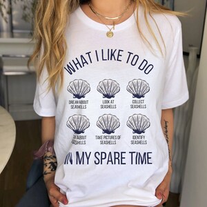 May include: White t-shirt with the text "What I like to do" and a series of seashells with text describing activities related to seashells, such as "Dream about seashells", "Look at seashells", "Collect seashells", "Talk about seashells", "Take pictures of seashells", and "Identify seashells". The text "In my spare time" is below the seashells.